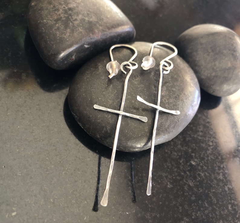 May include: A pair of silver earrings with a cross design. The earrings are made of thin wire and have a small bead at the top.