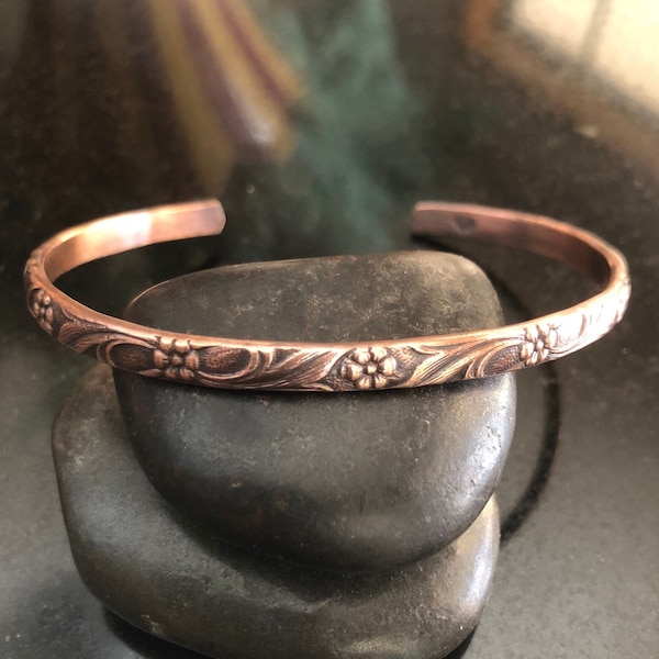 Pulseira rígida em cobre puro com design floral, ajustável, ideal para usar em conjunto com outras pulseiras, perfeita para presentear no 7º aniversário de casamento.