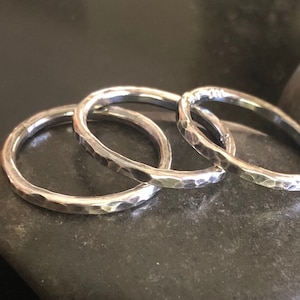 May include: Three silver hammered rings stacked on top of each other. The rings are all the same width and have a hammered texture.