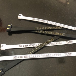 May include: Four white and black ring sizers with the text "SIZE & HALF SIZES" and numbers 1 through 17 printed on them. The sizers are marked "PAT. PEND. 9101693".