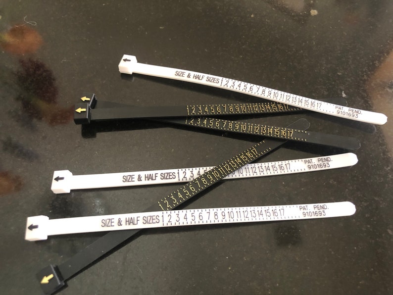May include: Four white and black ring sizers with the text "SIZE & HALF SIZES" and numbers 1 through 17 printed on them. The sizers are marked "PAT. PEND. 9101693".