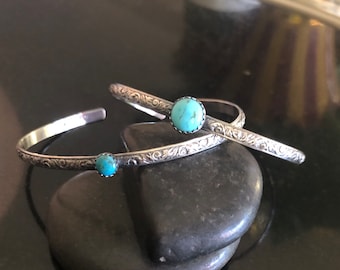 Pode incluir: Duas pulseiras de prata com pedras turquesa. As pulseiras são gravadas com um design floral.