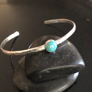 May include: A silver hammered bangle bracelet with a turquoise gemstone. The bracelet is open and has a simple design.