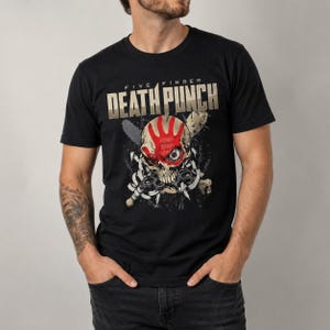 Könnte beinhalten: Ein schwarzes Kurzarm-T-Shirt mit einem Grafikdruck eines Schädels, der einen roten Handabdruck über dem Augenbereich aufweist. Der Text "FIVE FINGER DEATH PUNCH" ist in großen beigen Buchstaben über dem Schädel gedruckt, umgeben von Knochen.