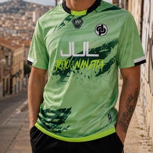 May include: A light green short-sleeve jersey with a dark green marbled pattern, a black crew neckline, and white sleeve cuffs. The front features the text JUL and TOTO & NINETTA, a 90 logo, and a circular emblem with the letters DP in black and white.