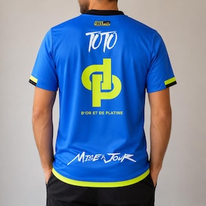 May include: A bright blue short-sleeved jersey with a black collar and lime green trim at the hem and sleeves. The back features the text 911, TOTO, D'OR ET DE PLATINE, and MISE À JOUR, along with a large lime green interlocking DP logo graphic.
