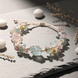 Peut inclure: Bracelet en macramé fait à la main, orné de pierres brutes d'aigue-marine et de quartz rose, agrémenté de perles florales aux couleurs pastel. Le bracelet réglable est réalisé avec un cordon crème, créant une esthétique bohème et naturelle.