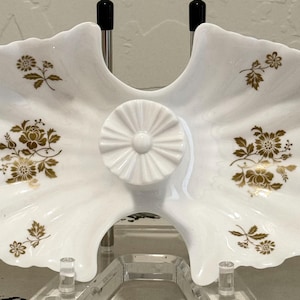 May include: A white milk glass divided serving dish with a ruffled edge and a central circular handle. The dish features a repeating gold floral pattern printed on both sides of the divider. The piece is supported by a clear acrylic stand.