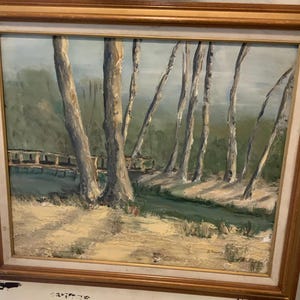 May include: Oil painting in a gold frame showing a tranquil landscape. Tall, thin trees with pale bark stand near a small bridge over a stream. The painting uses muted greens, blues, and browns, creating a peaceful scene.