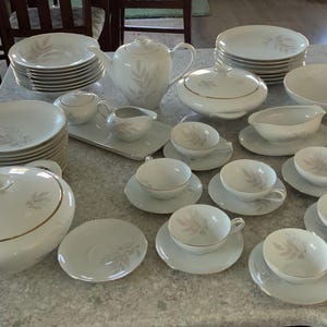 May include: A complete white porcelain dinnerware set with a leaf design. The set includes plates, bowls, cups, saucers, a teapot, a serving dish, and a gravy boat. The set is ideal for a formal dining experience.