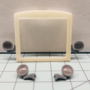May include: A collection of model car parts, including a rectangular frame, two circular side mirrors, and two headlights. The frame is off-white, the mirrors are gray, and the headlights are silver.