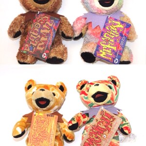 Puede incluir: Cuatro osos de peluche con diferentes patrones coloridos. Cada oso tiene una etiqueta con el nombre del oso, "Dancing Bear", "Peace Bear", "Cosmic Bear" y "Micky's Bear".