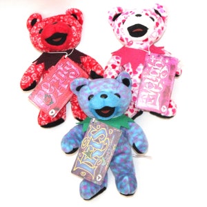 Puede incluir: Tres osos de peluche con diferentes patrones y colores. Los osos llevan collares de diferentes colores y tienen etiquetas que dicen "Pretty Please", "Everybody Loves" y "I Love You".