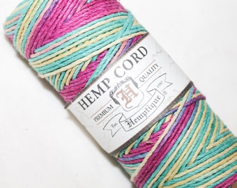 May include: A spool of colorful hemp cord with a label that reads "Hemptique Hemp Cord." The cord is a mix of pink, teal, and yellow. The label has the words "Premium Quality" and "Est. 1997."