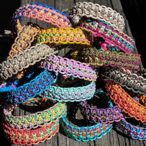 May include: A stack of colorful friendship bracelets made with woven string. The bracelets are in various colors, including pink, blue, green, yellow, and brown.