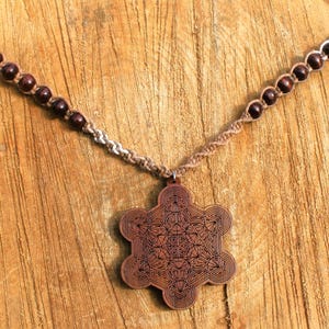May include: A brown wooden necklace with a geometric pattern pendant. The necklace is made of brown cord and brown wooden beads. The pendant is a star-shaped design with intricate details.