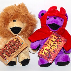 Puede incluir: Dos osos de peluche, uno con una melena de le&oacute;n marr&oacute;n y el otro con una capa roja y pelaje morado. El oso le&oacute;n tiene una etiqueta que dice "Mane Man" y el oso morado tiene una etiqueta que dice "Friend of Mine".