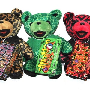 May include: Three plush teddy bears with different patterned fur. The bears are wearing black collars and have tags that say "Dark Star", "Steal Your Face", and "Grin" with a star.