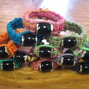 May include: A stack of eight colourful crocheted rings with black gemstone beads. Each ring is made with a different colour of yarn, including pink, blue, orange, green, purple, and grey.