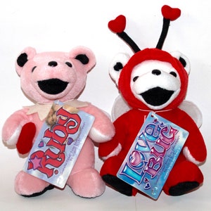 Puede incluir: Dos osos de peluche, uno rosa con un coraz&oacute;n y el texto "Ruby" en la etiqueta, y otro rojo con alas y el texto "Love Bug" en la etiqueta.