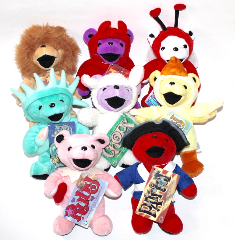 Puede incluir: Una colecci&oacute;n de nueve osos de peluche coloridos, cada uno con un disfraz diferente. Los osos est&aacute;n todos sonriendo y tienen una expresi&oacute;n juguetona. Los disfraces incluyen un le&oacute;n, un diablo, una mariquita, un pollo, un cordero, la Estatua de la Libertad, un pirata y un oso rosa con un coraz&oacute;n.