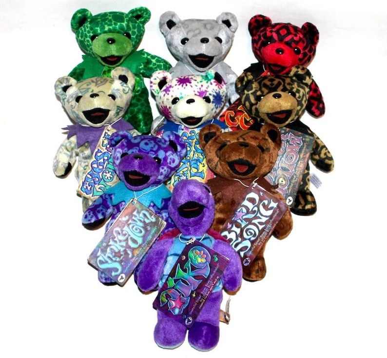 May include: A collection of ten colourful plush teddy bears with different patterns and designs. The bears are arranged in a heart shape with their tags visible. The tags feature the names of the bears, such as "Shakedown" and "Bird Song".