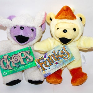Puede incluir: Dos osos de peluche con disfraces. Un oso lleva un disfraz de oveja blanco con la cara morada y la etiqueta "CHOPS Grateful Dead Bear by Liquid Blue" adjunta. El otro oso lleva un disfraz de pollo amarillo con el pico naranja y la etiqueta "FINKY Grateful Dead Bear by Liquid Blue" adjunta.