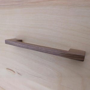 Op de afbeelding: Een rechthoekige, donkerbruine houten kastgreep.