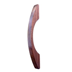 Puede incluir: Un tirador de mueble de madera maciza curvado con un rico patrón de vetas de color marrón oscuro. El tirador tiene un acabado liso y pulido con forma de arco semicircular, diseñado para montarse en puertas de muebles o cajones verticalmente.