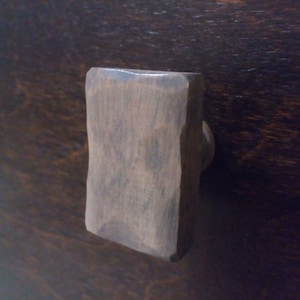 Peut inclure: Une poignée de tiroir rectangulaire en bois brun foncé avec une texture légèrement rugueuse.