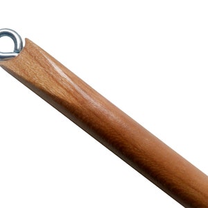 Puede incluir: Primer plano de una clavija de madera con una anilla metálica en el extremo. La clavija es de color marrón claro y tiene un acabado liso y pulido. La anilla es plateada y parece ser de metal. La clavija está en ángulo diagonalmente en el encuadre.