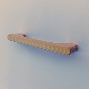 May include: A wooden drawer pull with a natural finish. The pull is curved and has a smooth surface.
