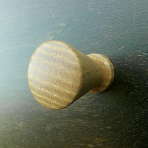 Puede incluir: Un pomo de madera de color marrón claro, ligeramente redondeado. El pomo tiene una superficie texturizada y está diseñado para usarse en armarios o cajones.