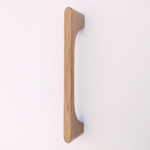 Peut inclure: Une poignée de porte de placard en bois avec une forme rectangulaire arrondie. La poignée est en bois brun clair et a une finition lisse.