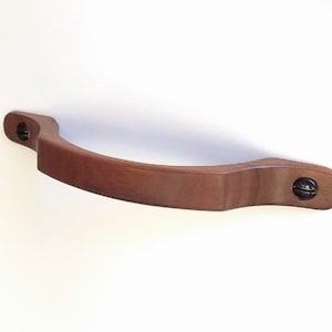 May include: A brown wooden cabinet pull with a curved shape and two black screws.