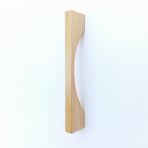 May include: A light wood cabinet pull with a curved design. The pull is made of solid wood and has a natural finish.