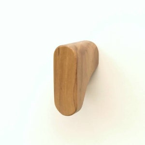 May include: A light brown wooden wall hook with a curved top and a rectangular base. The hook is made of solid wood and is mounted on a white wall. The hook is designed for hanging items.