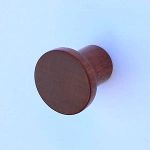 May include: A solid, dark brown wooden knob with a circular head and cylindrical base. The knob is likely for a cabinet or drawer, showcasing a minimalist design and natural wood grain.