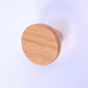 Può includere: Pomello per mobili in legno con una faccia arrotondata e circolare e una base cilindrica. Il pomello è realizzato in legno marrone chiaro, con venature visibili. Il pomello è progettato per armadi e cassetti.