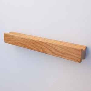 May include: A wooden wall-mounted shelf with a simple design. The shelf is made of natural oak wood and has a light brown color.
