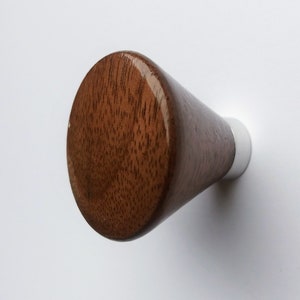 Puede incluir: Un tirador de armario de madera con forma cónica. El tirador es de madera marrón oscuro con un patrón de vetas visible y una base de metal plateado. El tirador está sobre un fondo blanco.