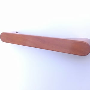 Puede incluir: Una manija de puerta de armario de madera con forma rectangular redondeada. La manija es de color marrón claro.