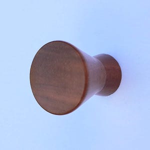May include: A wooden cabinet knob with a cylindrical design. The knob is a warm brown color and has a smooth, polished finish. The knob is designed to be mounted on a cabinet door or drawer.