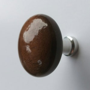 May include: A polished, oval-shaped wooden cabinet knob in a dark brown colour. The knob is attached to a silver-coloured metal base. Suitable for drawers and cabinets. The knob's dimensions are in centimetres.