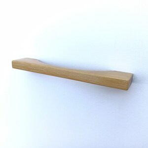 May include: A light brown wooden cabinet pull with a curved design.