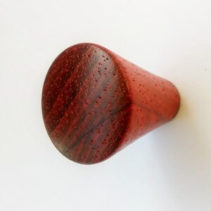 May include: A handcrafted, conical wooden knob with a rich, reddish-brown hue. The knob features a rounded top and a textured surface, showcasing the natural grain of the wood. This decorative element is suitable for furniture or cabinetry.