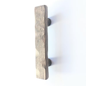 May include: A rustic wooden cabinet pull with a rough, textured surface and a dark brown finish. The pull has two metal knobs on the top and bottom.