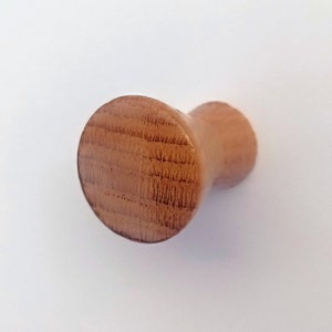 Puede incluir: Primer plano de un pomo de madera con la parte superior redondeada y una base cilíndrica. El pomo tiene un acabado de madera natural y una textura ligeramente rugosa.