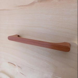 May include: A wooden cabinet pull with a rounded rectangular shape and a smooth, natural finish.