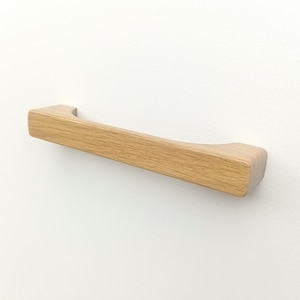 Könnte beinhalten: Ein hellbrauner, gebogener Holzknauf für Schränke. Der Knauf ist aus massivem Holz gefertigt und hat eine glatte Oberfläche.